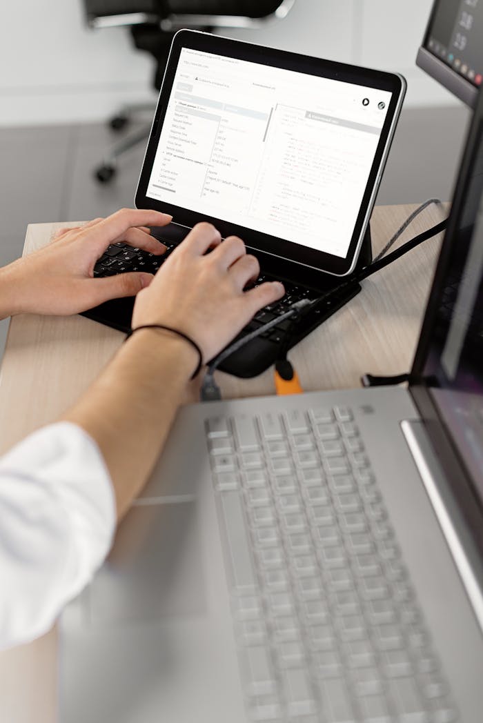 Close-up of hands typing on a laptop in an office setting, showcasing professional programming work.